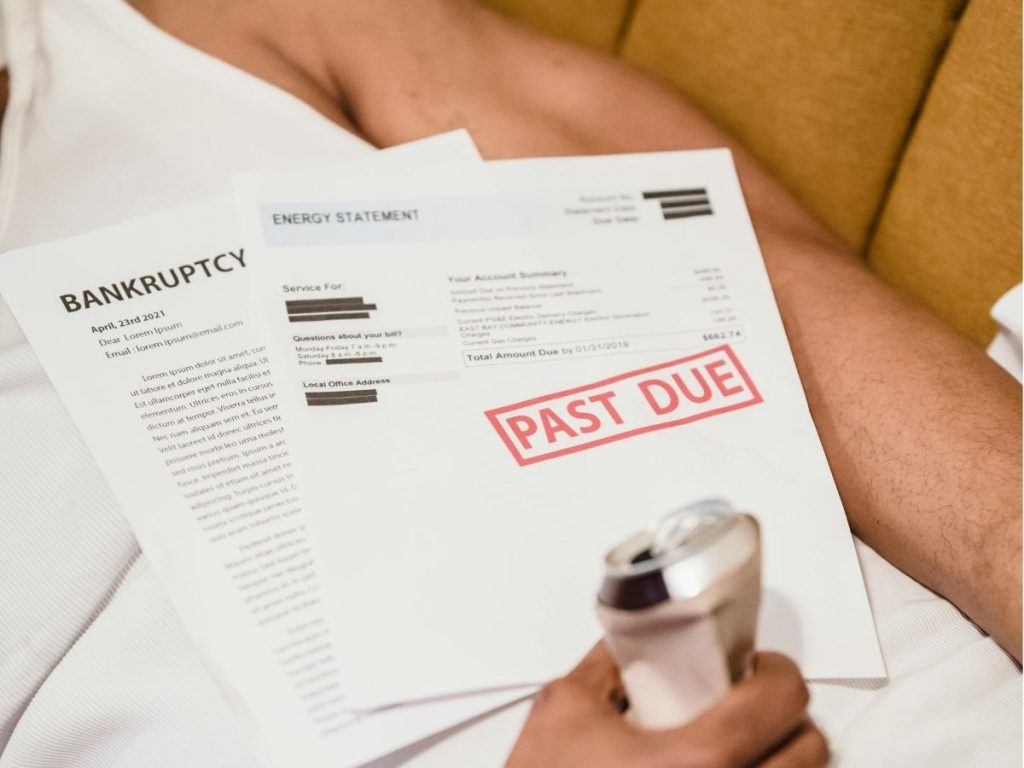 man lying down under unpaid bills holding a can